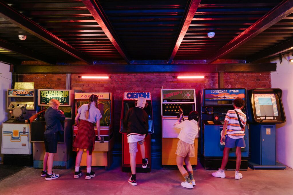 People playing vintage arcade games in a colorful room with exposed beams.