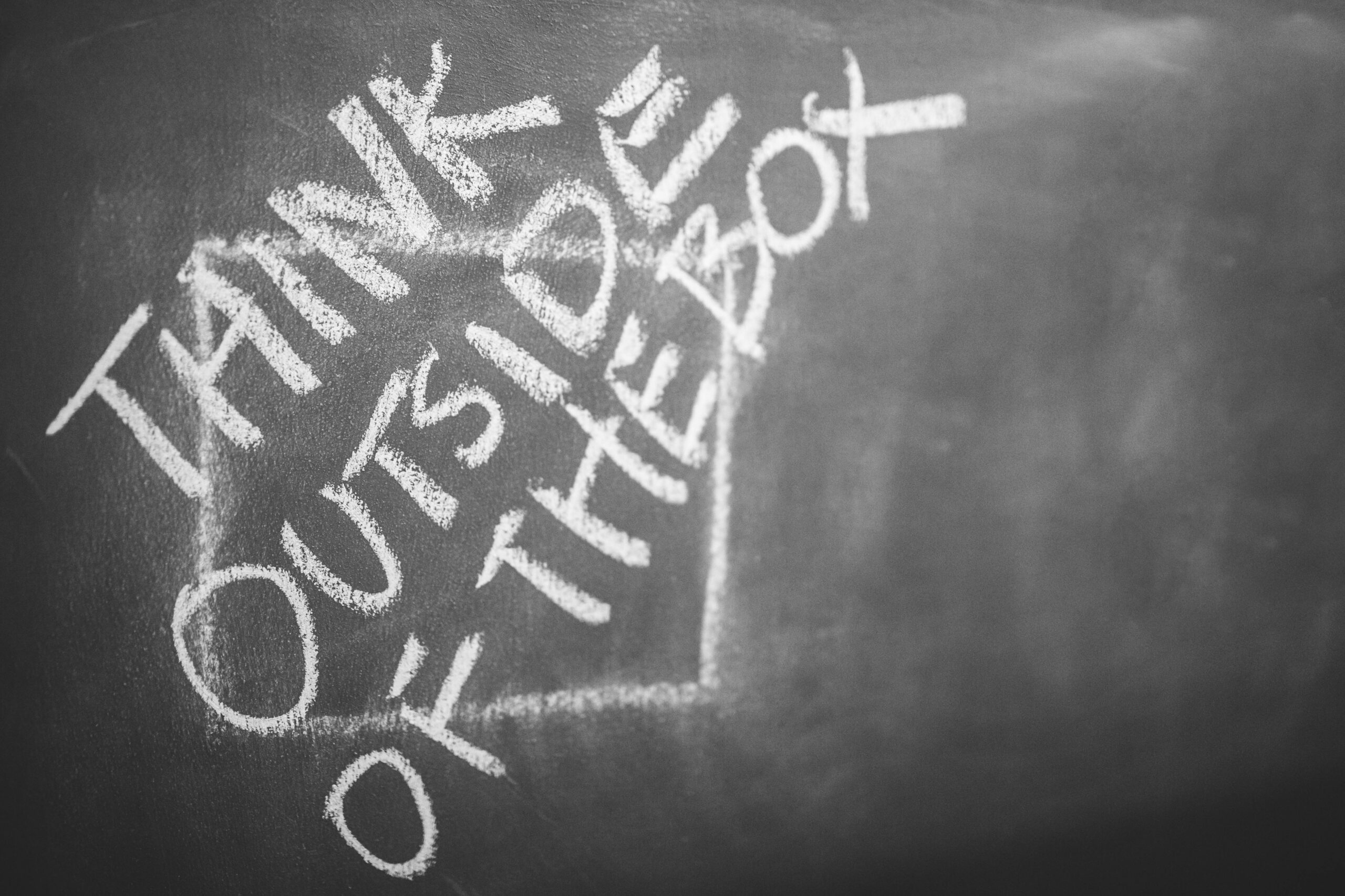 "Think Outside of the Box" written in white chalk on a blackboard.