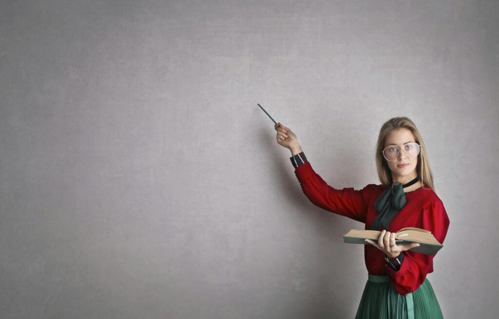 Person holding a book and pointing with a pen against a gray background.