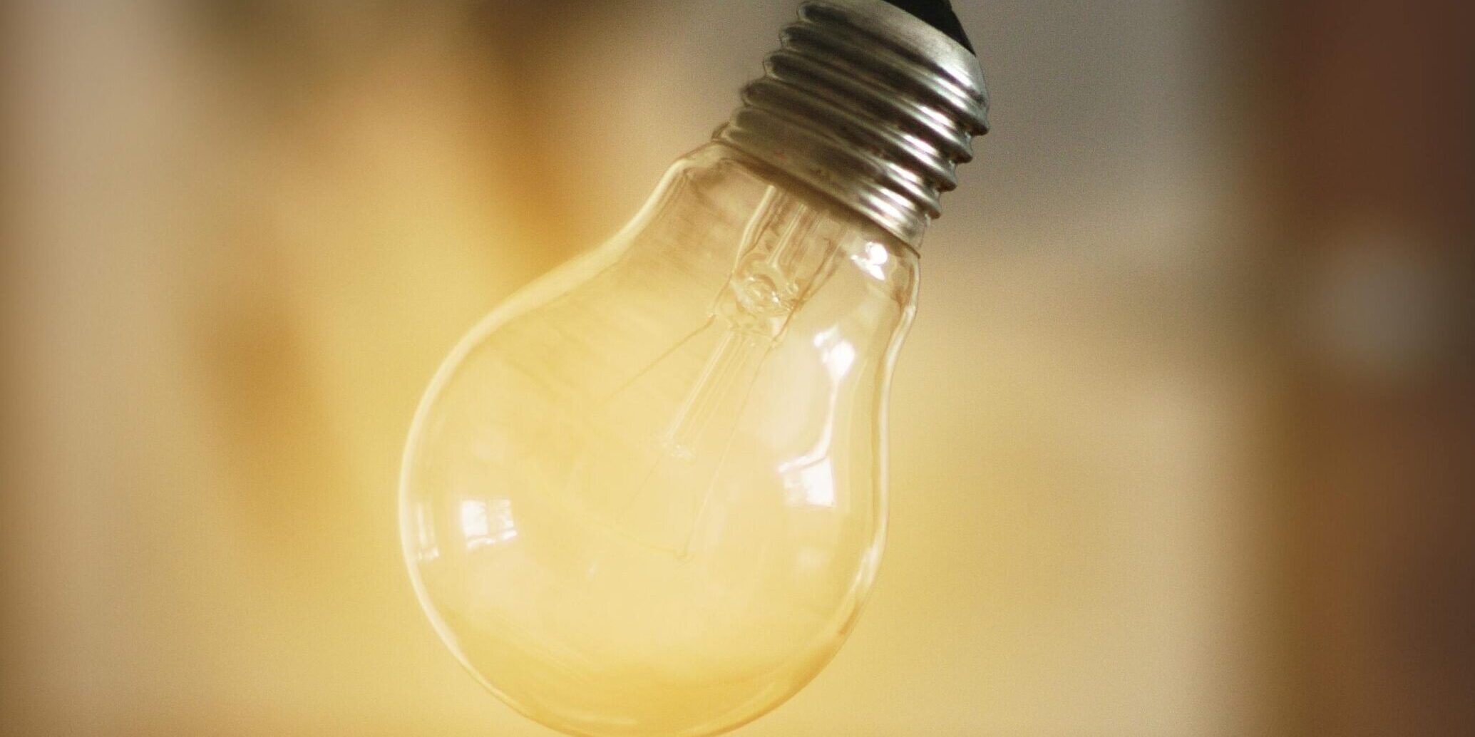 An illuminated lightbulb floating above an open palm, with a warm blurred background.