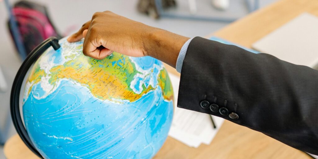A person in a suit pointing at a globe in a classroom setting.